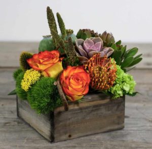 orange pincushion protea and orange and yellow roses with green accents