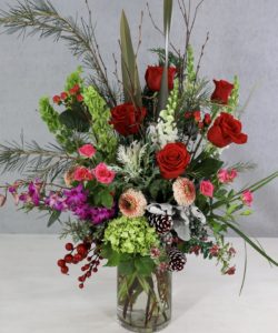 glass vase with lilies, orchids, roses, hydrangea and winter foliage and pine cones.