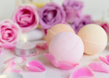 Pink and cream colored bath bombs on table with pink and lavender roses in background
