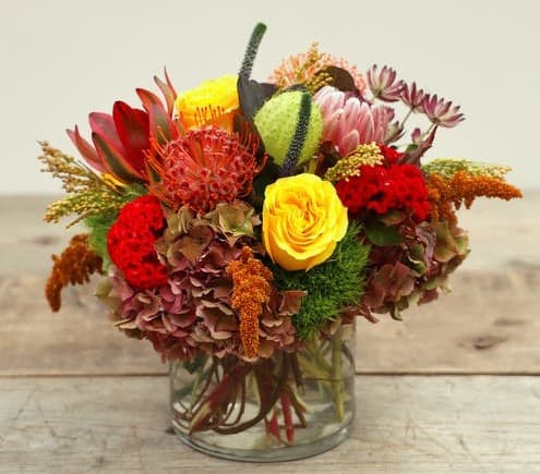 Celebrate the beauty of autumn with this eye-catching design, Amber Sunset. Featuring a beautiful selection of seasonal blooms of roses, hydrangea, protea and autumn textures to inspire. Finished with foliage in a glass vase.