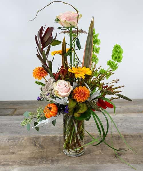 Splash your surroundings with modern artistry of festive Autumn colors with roses, carnations, kale, queen Anne's lace with harvest accents in a glass vase.