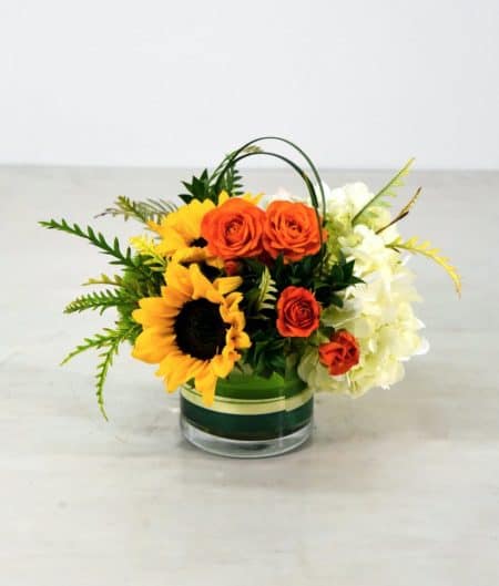 Today is the perfect day to let them know you're thinking of them. A cheery design of colorful sunflowers, spray roses and hydrangea in ribbon lined glass vase. 